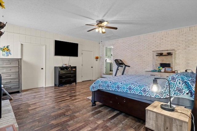 bedroom featuring brick wall, attic access, wood finished floors, a textured ceiling, and a ceiling fan