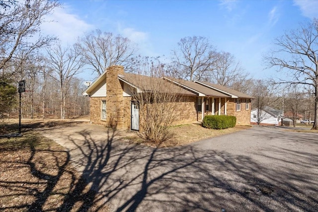 view of side of property with aphalt driveway, brick siding, and a chimney