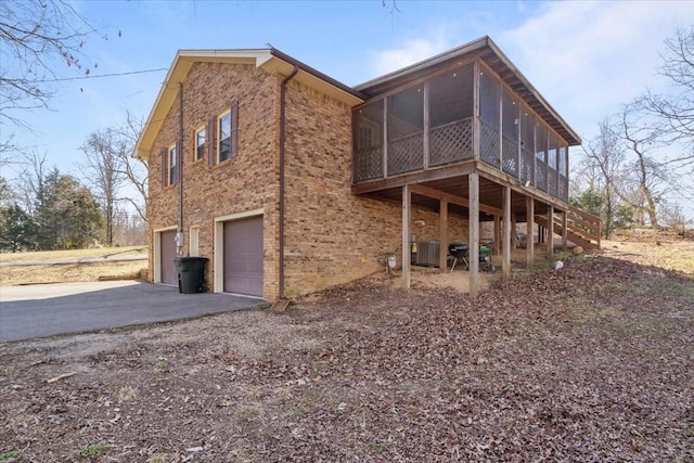 rear view of property with brick siding, aphalt driveway, central air condition unit, a garage, and a sunroom