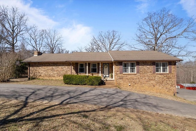 ranch-style house featuring driveway, brick siding, and a chimney