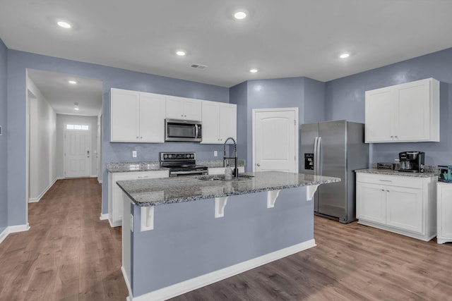 kitchen featuring visible vents, a center island with sink, appliances with stainless steel finishes, stone countertops, and a sink