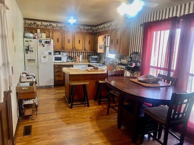 kitchen with visible vents, a textured ceiling, white refrigerator with ice dispenser, a peninsula, and light countertops