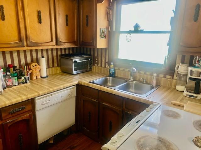 kitchen with a toaster, dishwasher, light countertops, electric stove, and a sink