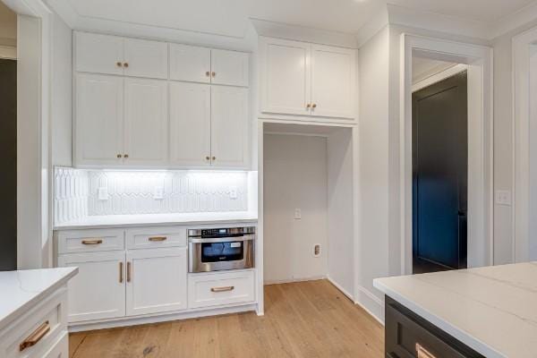 kitchen with white cabinetry, stainless steel oven, light wood-style flooring, and light stone countertops