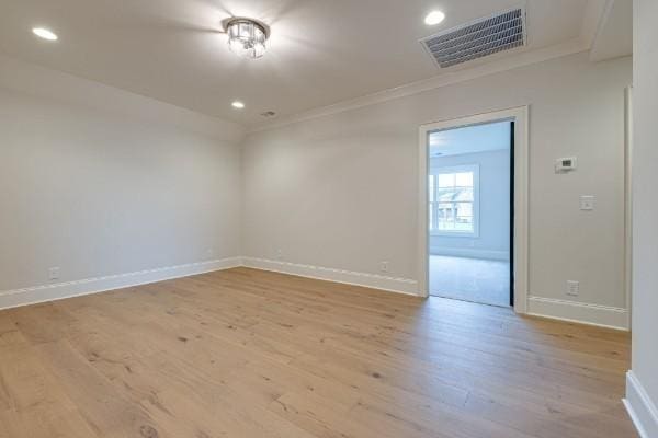 spare room featuring ornamental molding, light wood-style floors, visible vents, and baseboards