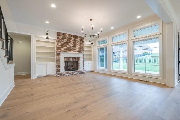 unfurnished living room with built in features, light wood-style flooring, recessed lighting, stairs, and a brick fireplace