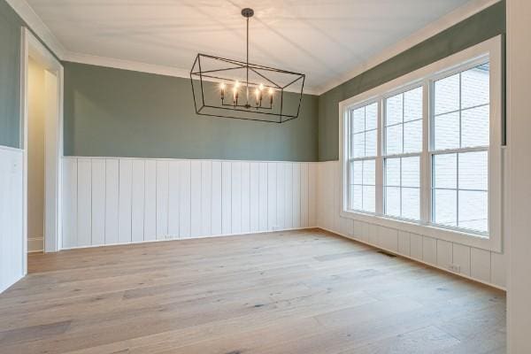 unfurnished room with an inviting chandelier, wood finished floors, wainscoting, and crown molding