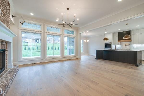 kitchen featuring an inviting chandelier, ornamental molding, oven, a brick fireplace, and open floor plan