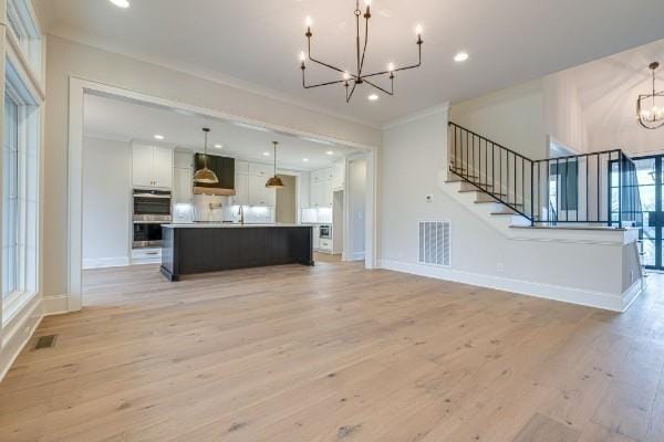 unfurnished living room featuring light wood-style floors, visible vents, a notable chandelier, and stairway