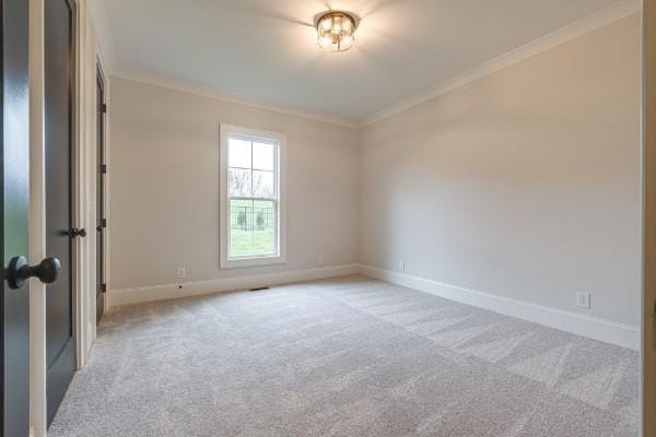 spare room featuring light carpet, crown molding, and baseboards