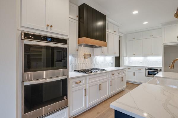 kitchen with light stone counters, decorative backsplash, light wood-style floors, appliances with stainless steel finishes, and white cabinetry