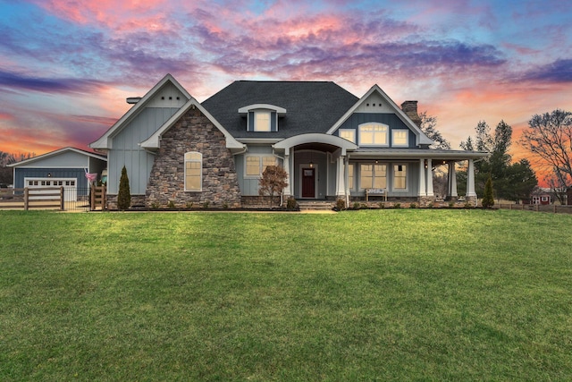 view of front of house with board and batten siding, fence, stone siding, and a lawn