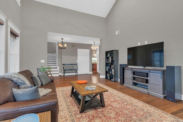 living area with stairs, a notable chandelier, wood finished floors, and high vaulted ceiling