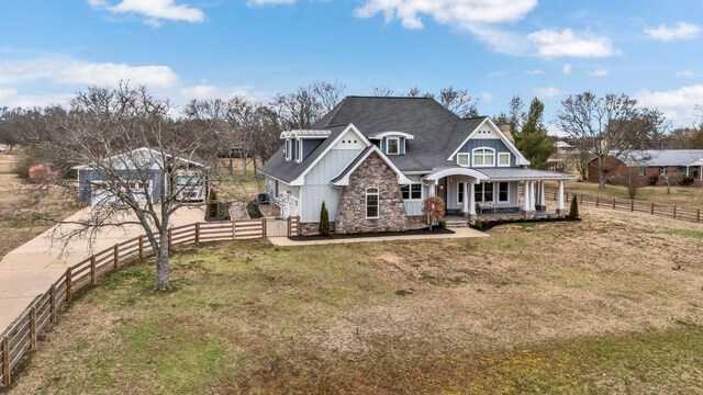 view of front facade featuring board and batten siding, fence, a porch, a front yard, and stone siding