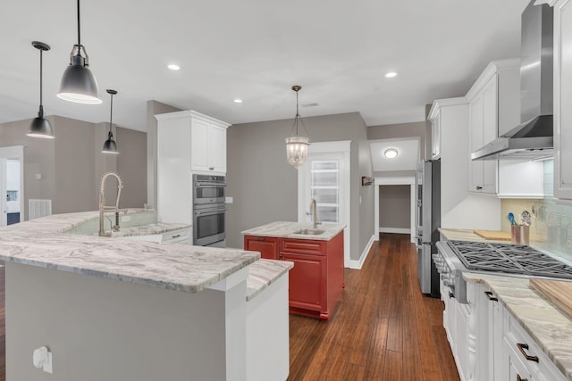 kitchen featuring an island with sink, a sink, stainless steel appliances, wall chimney range hood, and decorative backsplash