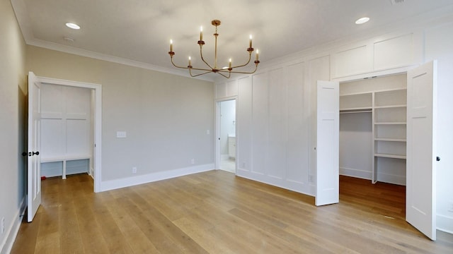 unfurnished bedroom with a walk in closet, light wood-type flooring, ornamental molding, a closet, and a notable chandelier