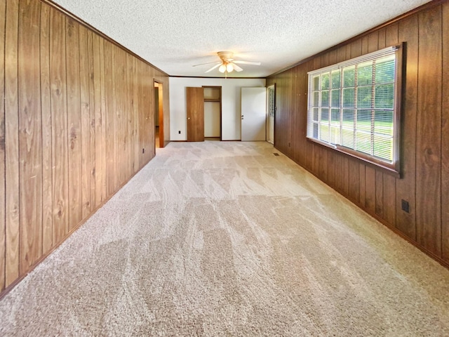 carpeted spare room with crown molding, wooden walls, a ceiling fan, and a textured ceiling