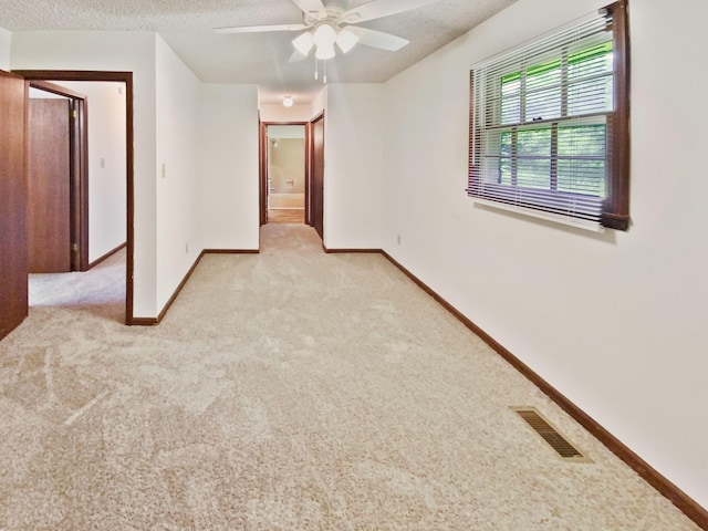 spare room featuring visible vents, a textured ceiling, baseboards, light colored carpet, and ceiling fan