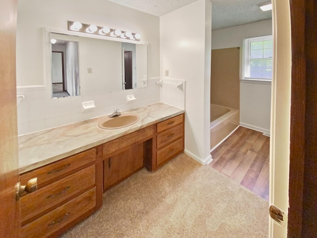 full bath with a bathing tub, a textured ceiling, wood finished floors, baseboards, and vanity