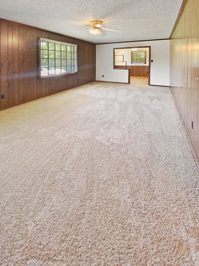 unfurnished living room featuring wooden walls, carpet, a ceiling fan, and a textured ceiling