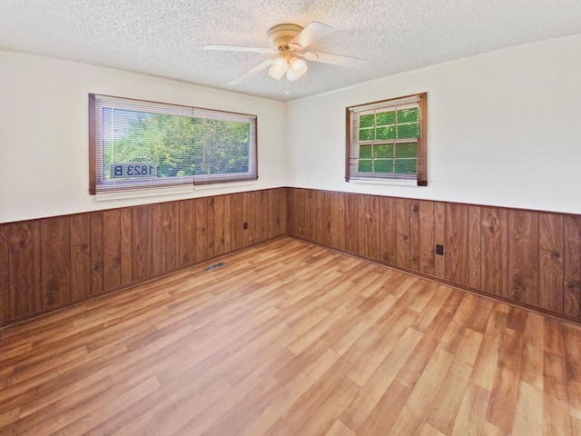 spare room featuring light wood-type flooring, a wainscoted wall, a textured ceiling, and wood walls