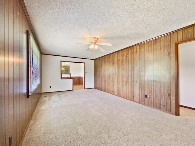 unfurnished room featuring a ceiling fan, a textured ceiling, wood walls, crown molding, and light colored carpet