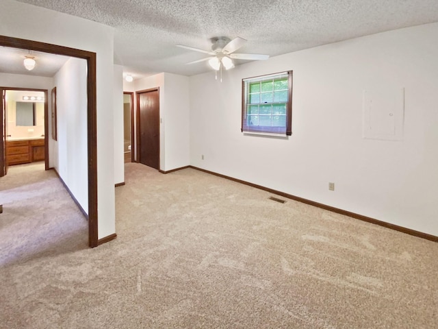 spare room featuring a textured ceiling, a ceiling fan, baseboards, and light carpet