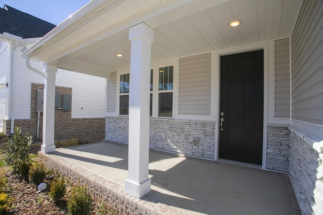 view of exterior entry with stone siding, a porch, and roof with shingles