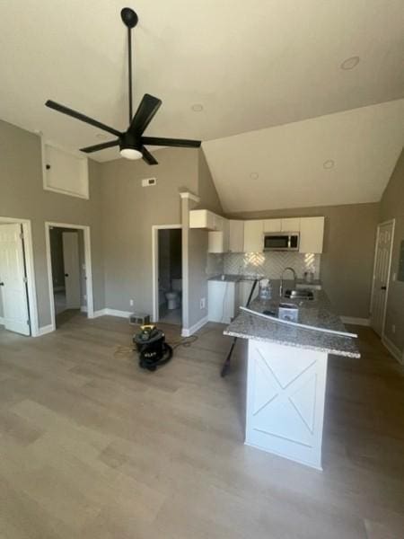 kitchen with stainless steel microwave, backsplash, white cabinetry, and baseboards