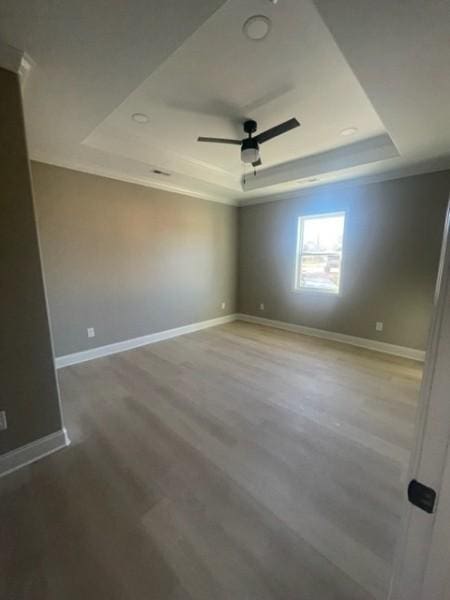 spare room featuring wood finished floors, baseboards, a tray ceiling, and a ceiling fan