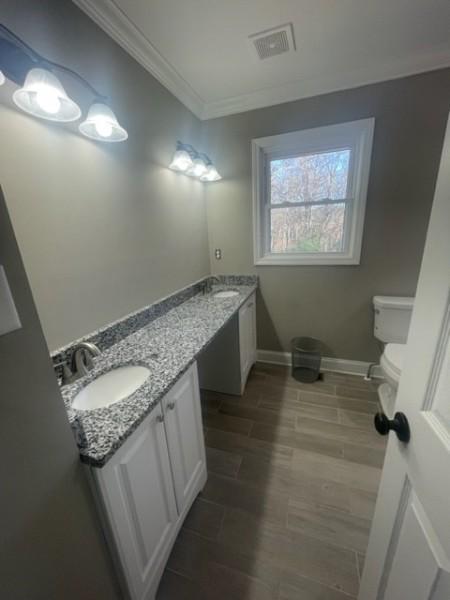 bathroom with visible vents, ornamental molding, a sink, wood finished floors, and double vanity