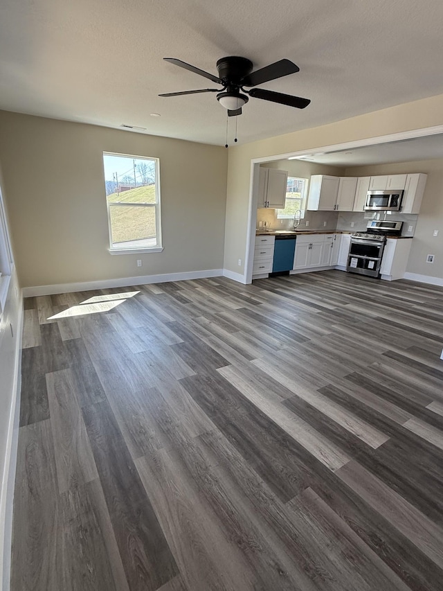 unfurnished living room with a ceiling fan, baseboards, dark wood finished floors, a sink, and a textured ceiling