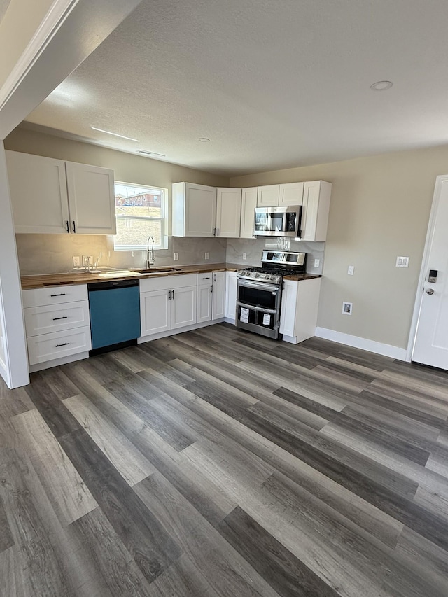 kitchen featuring decorative backsplash, appliances with stainless steel finishes, white cabinets, wood counters, and a sink