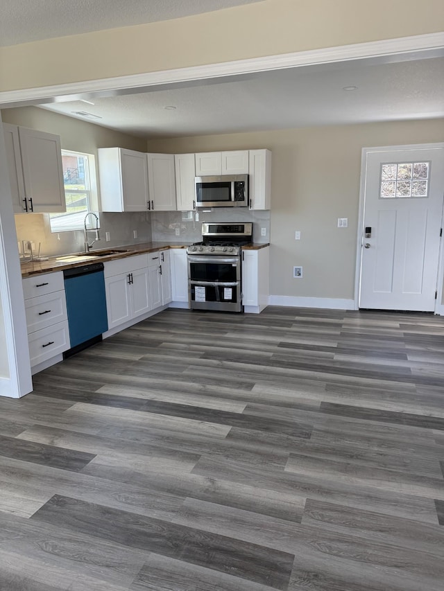 kitchen featuring a sink, stainless steel appliances, dark wood-type flooring, white cabinets, and tasteful backsplash