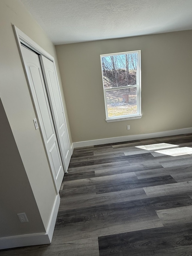 unfurnished bedroom featuring a closet, baseboards, a textured ceiling, and dark wood finished floors