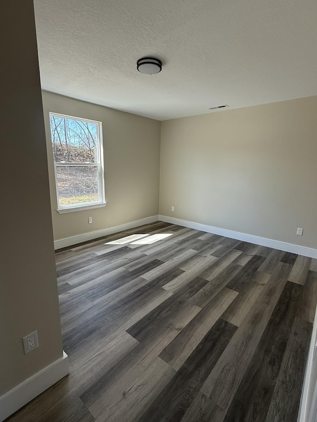 spare room featuring dark wood finished floors, baseboards, visible vents, and a textured ceiling