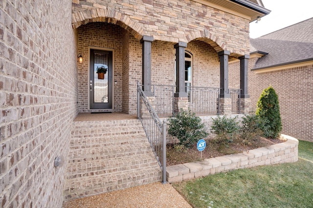 entrance to property featuring brick siding, stone siding, covered porch, and a shingled roof