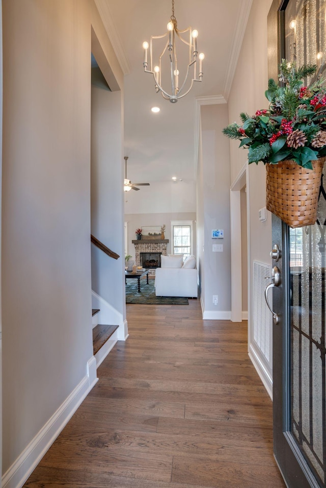 foyer entrance featuring wood finished floors, baseboards, a fireplace, stairs, and crown molding