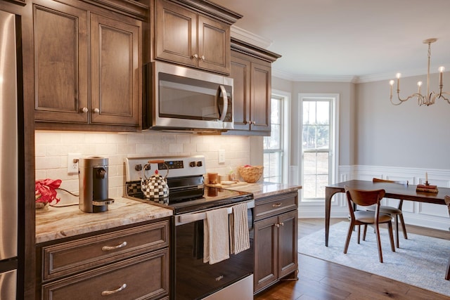 kitchen with a wainscoted wall, ornamental molding, tasteful backsplash, stainless steel appliances, and dark wood-style flooring