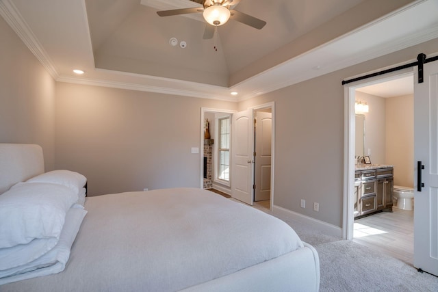 bedroom with light carpet, connected bathroom, a tray ceiling, and a barn door