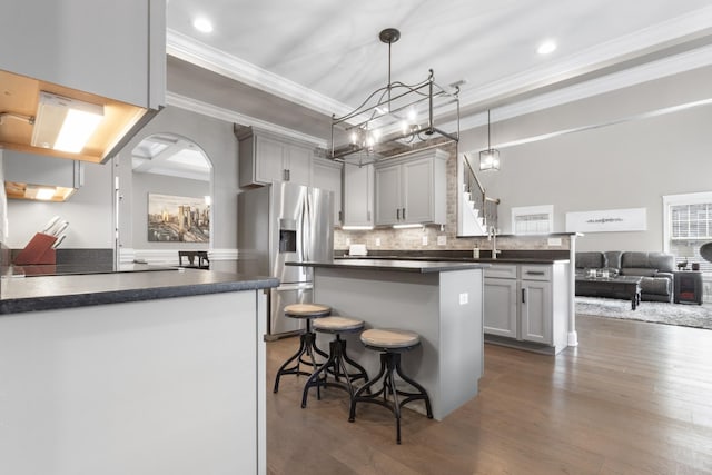 kitchen with dark wood-style floors, a peninsula, dark countertops, a notable chandelier, and stainless steel fridge