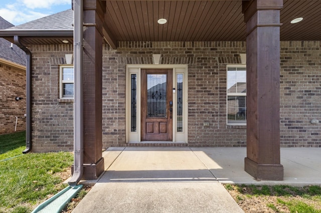 doorway to property with brick siding and roof with shingles