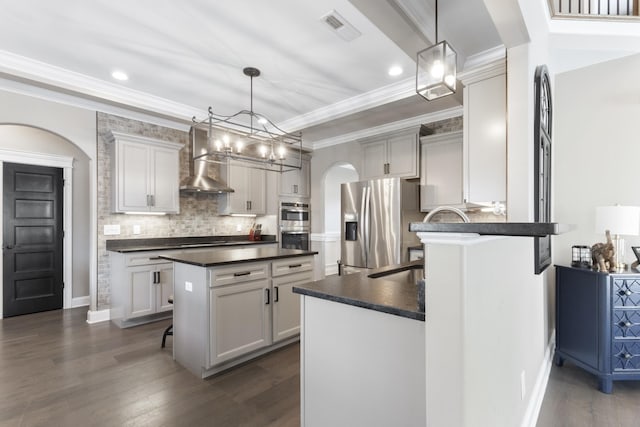 kitchen with dark countertops, wall chimney exhaust hood, arched walkways, and stainless steel appliances