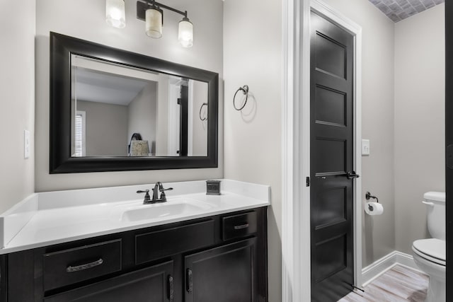 half bathroom featuring toilet, vanity, and baseboards