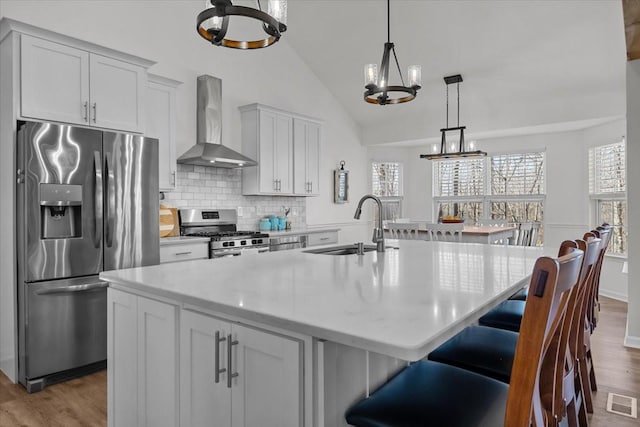 kitchen featuring a sink, light countertops, appliances with stainless steel finishes, wall chimney exhaust hood, and a chandelier