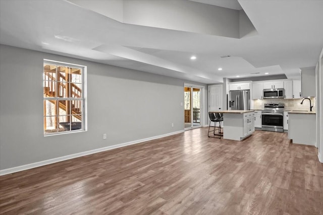 unfurnished living room with a raised ceiling, a sink, wood finished floors, recessed lighting, and baseboards