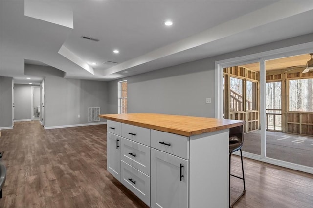 kitchen featuring wood counters, a kitchen bar, white cabinets, and dark wood-style flooring