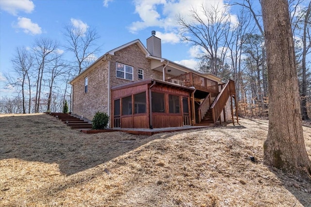 back of property with a wooden deck, a chimney, stairs, and a sunroom