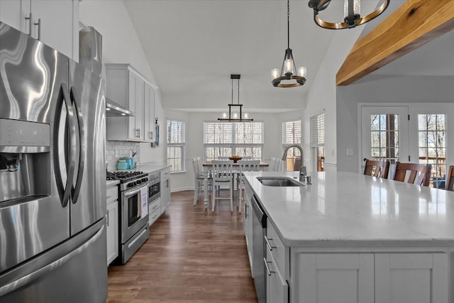 kitchen with tasteful backsplash, vaulted ceiling with beams, appliances with stainless steel finishes, a notable chandelier, and a sink