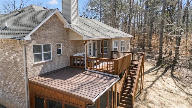 rear view of house featuring brick siding, a wooden deck, stairs, roof with shingles, and a chimney